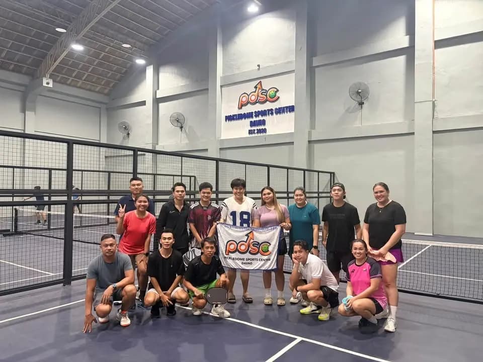 Pickledome players posing with a banner beside the courts